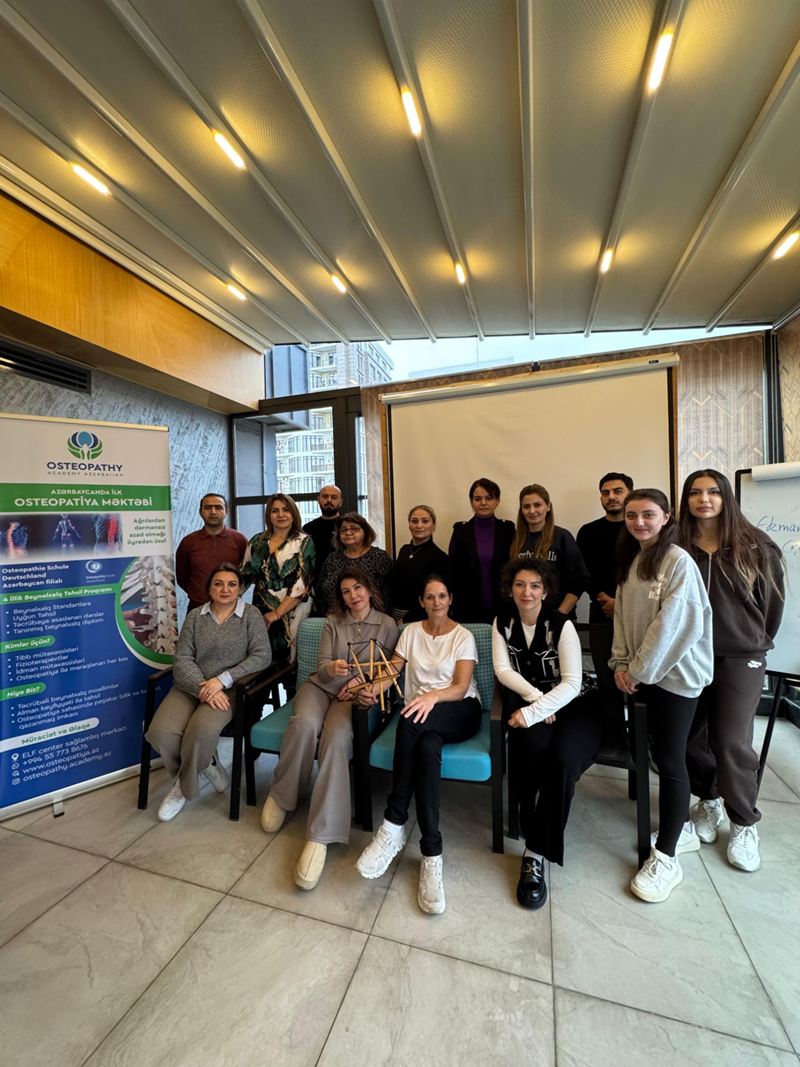 Tələbələr və müəllim akademiyanın banneri önündə; müəllimin əlində tensegrasiya modeli var.